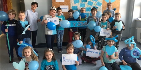 Powiększ grafikę: Uczniowie klasy I, ubrani na niebiesko wraz z wychowawczynią i Panią Dyrektor pozują na tle gazetki o autyzmie, w rękach trzymają niebieskie balony