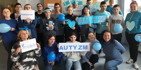 Powiększ grafikę: Uczniowie klasy VIII, ubrani na niebiesko pozują na tle gazetki o autyzmie, w rękach trzymają niebieskie balony oraz napis AUTYZM