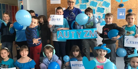Powiększ grafikę: Uczniowie klasy I, ubrani na niebiesko wraz z wychowawczynią pozują na tle gazetki o autyzmie, w rękach trzymają niebieskie balony oraz duży napis AUTYZM
