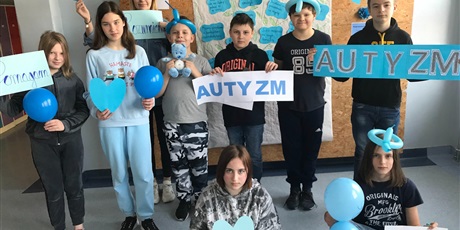 Powiększ grafikę: Uczniowie klasy VI, ubrani na niebiesko pozują na tle gazetki o autyzmie, w rękach trzymają niebieskie balony oraz napis AUTYZM