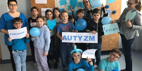 Powiększ grafikę: Uczniowie klasy III, ubrani na niebiesko pozują na tle gazetki o autyzmie, w rękach trzymają niebieskie balony oraz napis AUTYZM