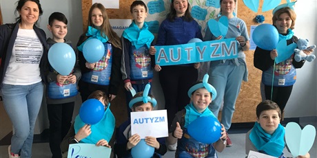 Powiększ grafikę: Uczniowie klasy V, ubrani na niebiesko pozują na tle gazetki o autyzmie, w rękach trzymają niebieskie balony oraz napis AUTYZM