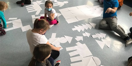 Powiększ grafikę: Uczniowie klasy I układają na holu figury, korzystając z wycietych kół, kwadratów, trójkątów